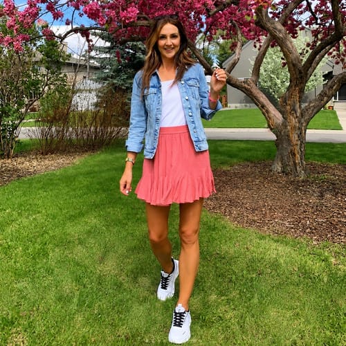 Reviewer standing outdoors wearing white Cosmos walking shoes with a pink skirt and denim jacket.