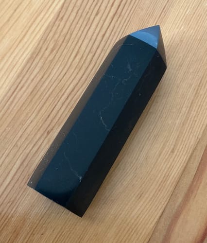 Pointe de Shungite polie d'un client, posée sur une surface en bois.