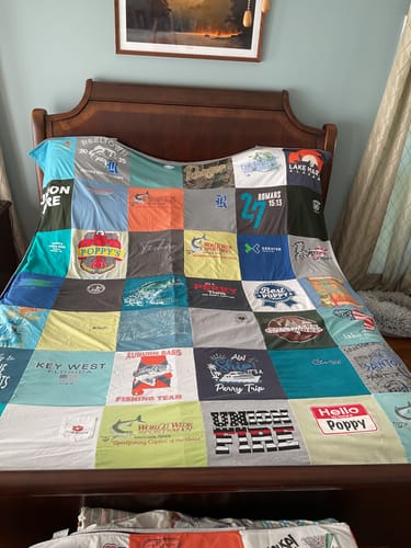 Customer's Project Repat T-Shirt Quilt, a colorful patchwork of shirts, spread across a bed.