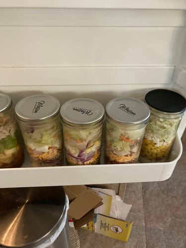 Customer's fresh salads meal-prepped in sealed Mason jars and stored in a refrigerator door.