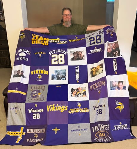 Customer holding up a large Project Repat T-Shirt Quilt made from purple and grey Minnesota Vikings shirts.