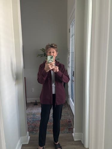 Reviewer taking a mirror selfie wearing the toasted garnet Ryann Hoodie, fully zipped.