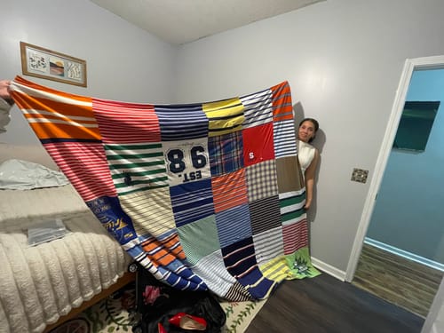 Customer holding up a large, colorful Project Repat T-Shirt Quilt in a bedroom.