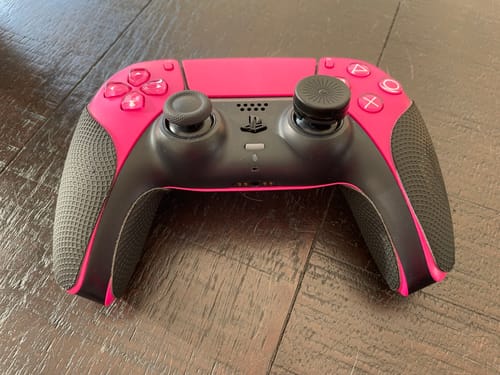 Ein Kunde zeigt die schwarzen RZ Controller Grips auf einem pinken PS5-Controller, der auf einem Holzboden liegt.