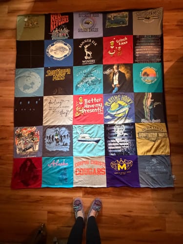 Customer's completed Project Repat T-Shirt Quilt made from colorful shirts, spread out fully on a wood floor.