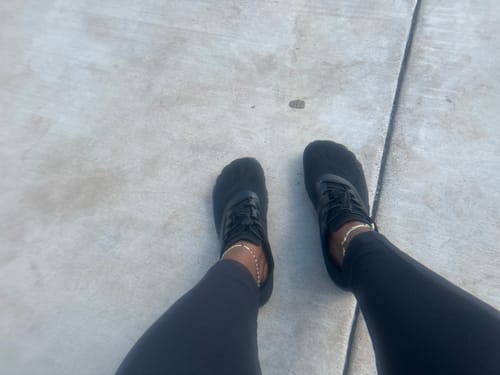 A reviewer's view looking down at their black Smart Ⅰ - Barefoot Shoes while standing outside on pavement.