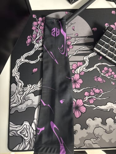 Ein Kunde zeigt den RZ Arm Sleeve in der schwarz-lila Edition, flach auf einem Schreibtischpad liegend.