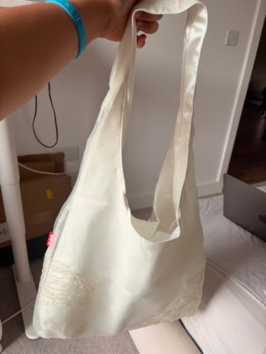 Customer holding the white, sheer BTS Shoulder Bag up in a room.