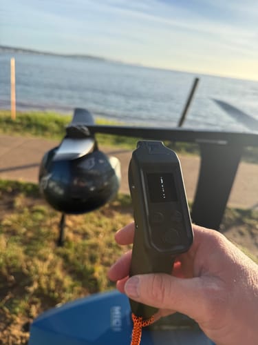 Reviewer holding the black Foil Drive V3 Throttle Controller, with a hydrofoil board and water in the background.