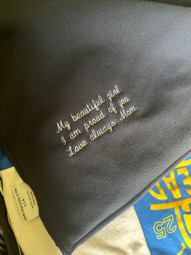 Close-up of a reviewer's T-Shirt Quilt showing the custom embroidered message on the dark fleece backing.