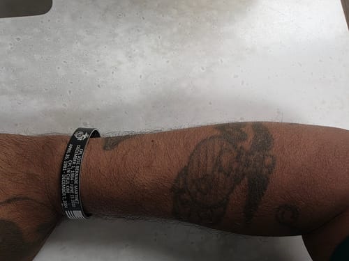 A customer wearing their custom black bracelet on their wrist, showing the engraved text and military emblems.