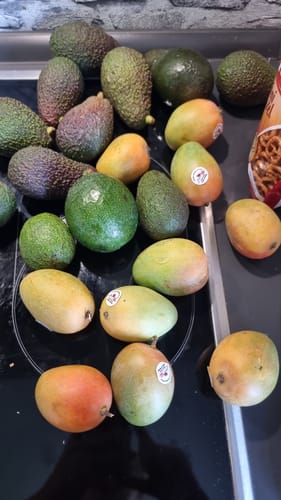 Rezensent zeigt die erhaltenen Baby-Zuckermangos und Avocados auf einer schwarzen Herdplatte ausgebreitet.
