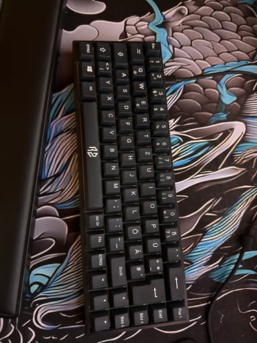 Kundenfoto der kompakten, schwarzen RZ 65 HE Gaming-Tastatur, die auf einer gemusterten Schreibtischunterlage liegt.