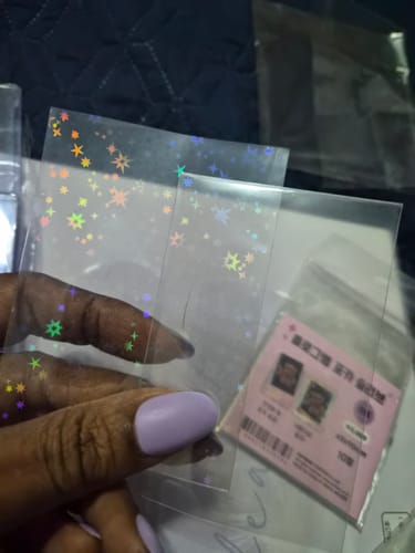 Close-up of a customer's hand holding clear Premium Photocard Sleeves, one with a holographic star pattern.