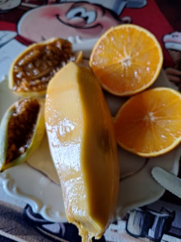 Rezensent zeigt eine geschälte, saftige Nam Dok Mai Mango neben Orangenhälften auf einem Teller.