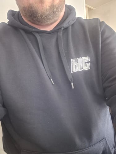 Gros plan d'un client portant le sweat à capuche noir HC Argenté, montrant le logo brodé.