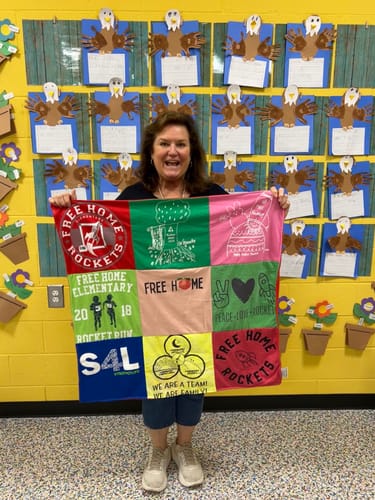 Customer holding a colorful 9-panel Project Repat T-Shirt Quilt made from school-themed shirts.
