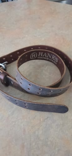 Customer's brown leather Woodstock belt coiled on a surface, showing the double-punched holes along its length.