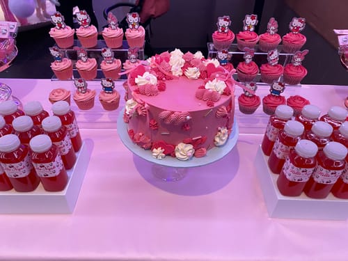 Reviewer's decorated Pretty In Pink Cake on a stand, displayed on a dessert table for a birthday party.