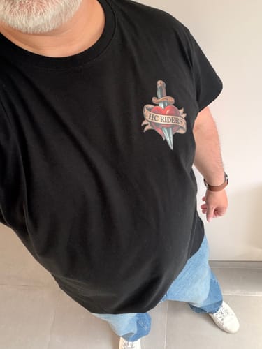 Client portant le T-shirt Riders noir, avec le logo d'un cœur et d'une dague sur la poitrine.