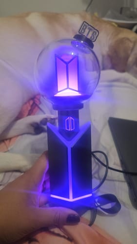 Customer holding the BTS Official Light Stick Ver.4 and cradle, both glowing with a bright purple light.