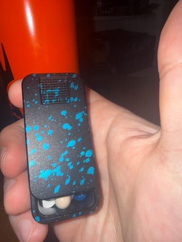 Customer holding a black and blue splatter Nano Case, which is open and contains pills.