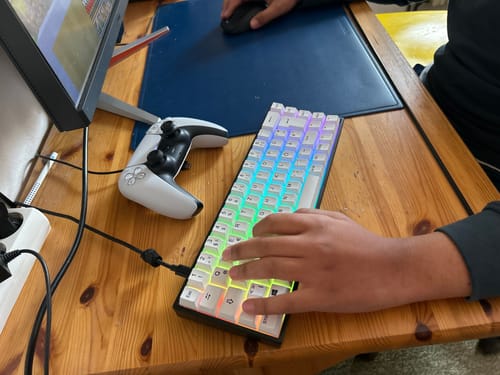 Ein Kunde benutzt die RZ Gaming-Tastatur - RZ 65 HE mit farbenfroher Beleuchtung auf einem Holzschreibtisch.