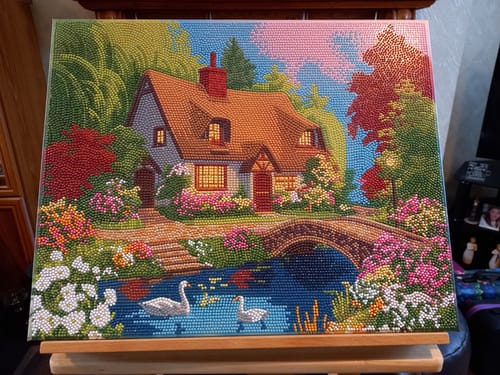 Customer's completed Cosy Cottage Crystal Art canvas, a sparkling picture of a cottage, bridge, and pond with two swans.