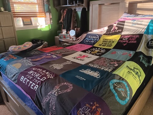 Customer's colorful Project Repat T-Shirt Quilt, made of many different shirts, spread across a bed in a bedroom.