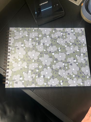 Customer's spiral-bound Nancy Planner with the floral Moonblossom cover lying on a dark desk.