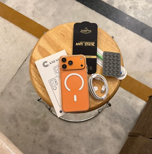 Customer's new orange Magsafe case displayed on a wooden stool with its packaging and a white cable.