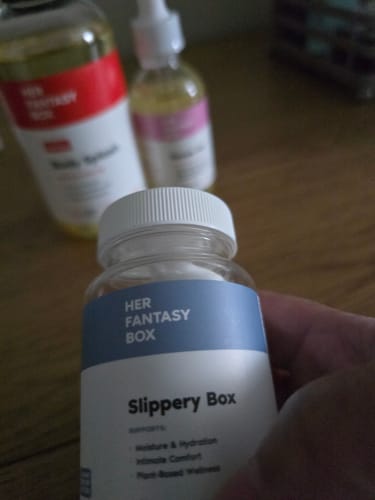 Customer's hand holding the Slippery Box bottle from the Moisture Support + Hydration Kit, with other kit items in the background.