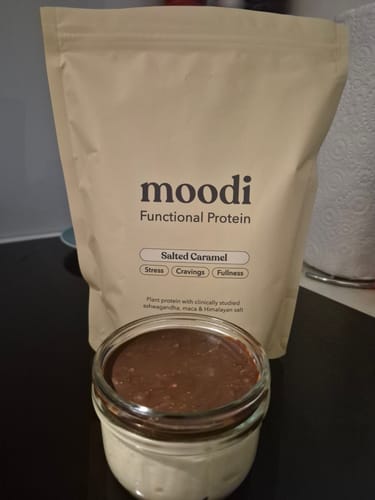 Customer's Salted Caramel protein powder bag shown behind a creamy yogurt bowl with a chocolate topping.