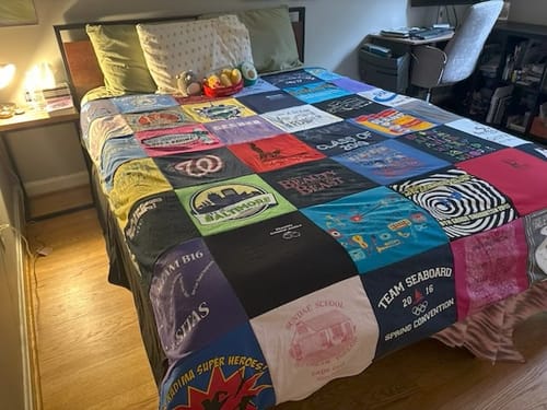 A customer's colorful Project Repat T-Shirt Quilt, made from many t-shirts, spread across a bed in a bedroom.