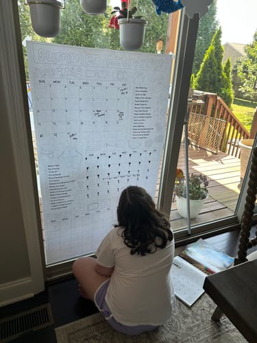 Reviewer shows a person looking at the large Summer Activity Calendar Coloring Sheet taped to a window.