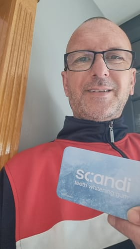 Reviewer smiling while holding up a pack of scandi teeth whitening gum.