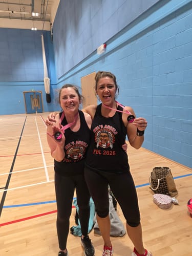 Two reviewers in matching black racer back tanks celebrating with medals in a gym.