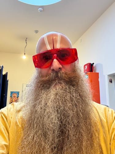 Reviewer with a long beard taking a selfie while wearing red VisionX glasses indoors.