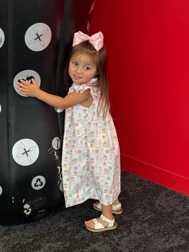 Customer wearing the Birthday Party Smocked Angel Sleeve Dress next to a large display object.