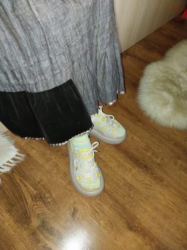 Close-up of a customer wearing the white and yellow leather platform sandals indoors on a wood floor.