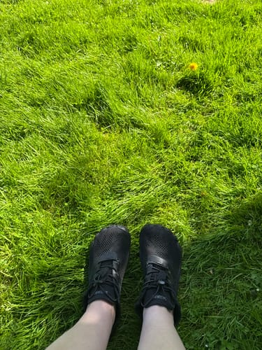 Reviewer wearing black Smart Ⅰ - Barefoot Shoes while standing on green grass.
