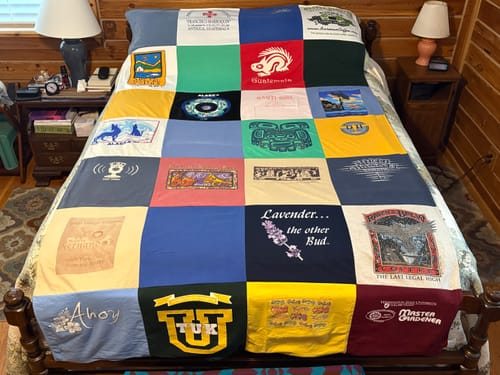 Customer's colorful Project Repat T-Shirt Quilt made from many different shirts, spread neatly across a bed in a bedroom.