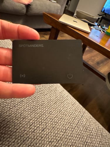 Customer holding the black SPOTMINDERS. Tracking Card in their hand in a living room.