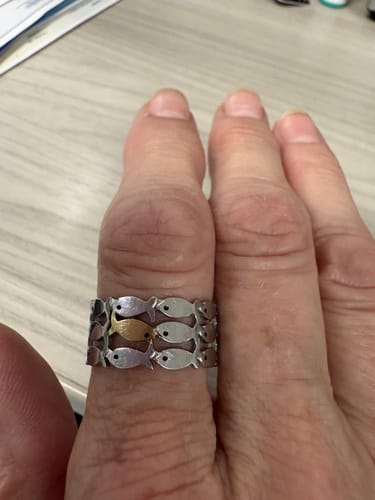 A reviewer's hand wearing the Swim Against The Current Ring, showing the design of one gold fish among rows of silver fish.