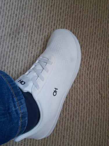 Kunde trägt einen weißen Prime Slip-On mit Jeans auf einem Teppich.