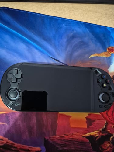 Consola Anbernic RG Vita Pro de un cliente, con la pantalla apagada, sobre un mousepad.