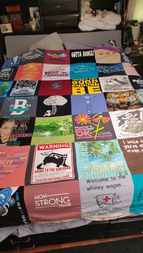 Customer's colorful Premium T Shirt Quilt, made from various t-shirts, spread out on a bed.