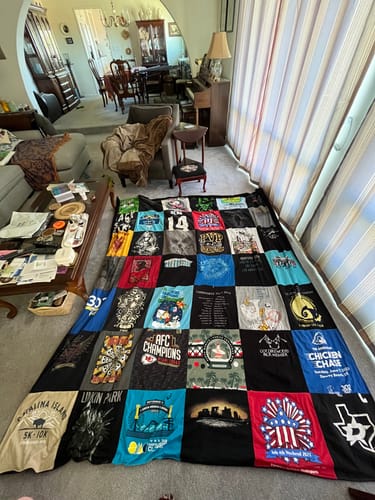 Customer's large, colorful T-Shirt Quilt spread out on a living room floor, showing many different shirt designs.