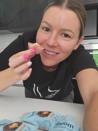 Reviewer smiling and holding a half-eaten Plant Protein Ball, with several more in their packaging on the counter.