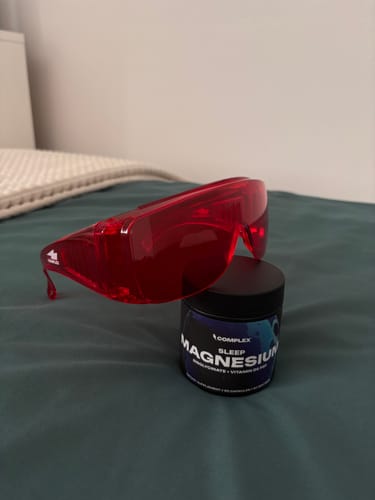 Customer's red VisionX glasses resting on a bed next to a jar of Complex magnesium.